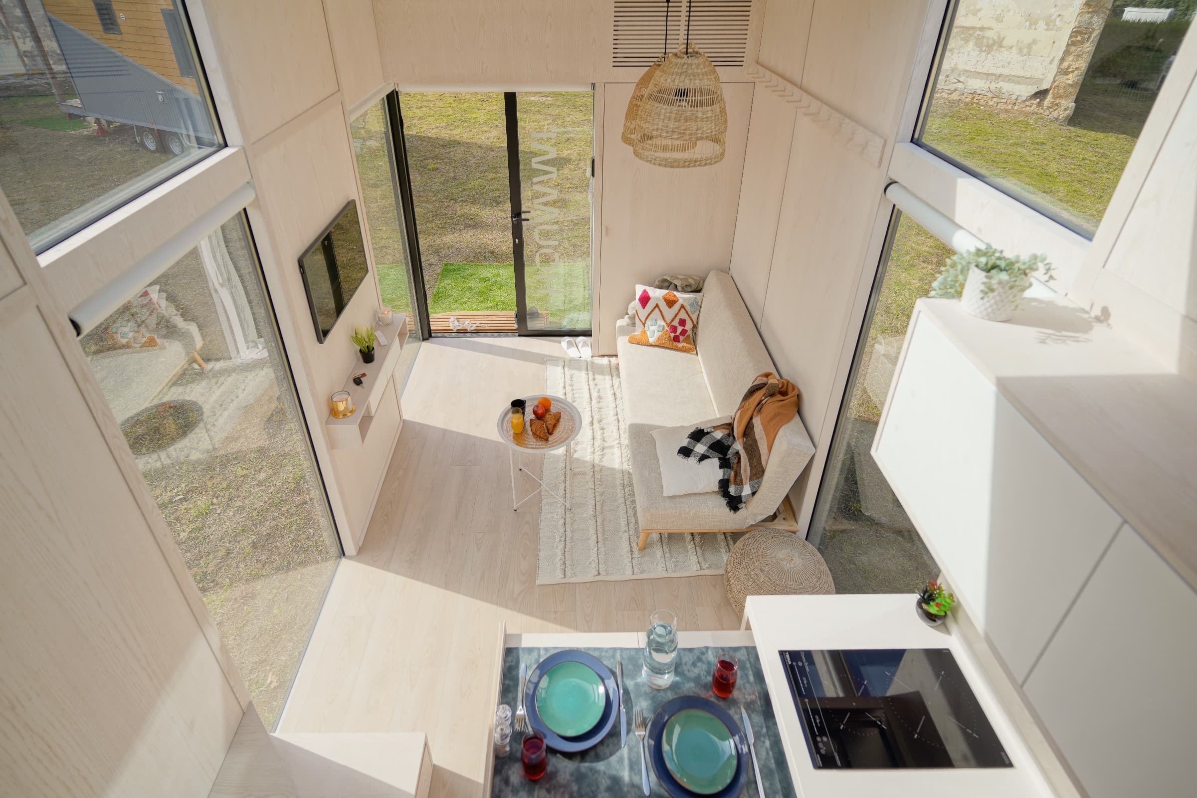 Intérieur d'un module Hoummi Home vu en plongée : séjour, coin repas dressé et baies vitrées ouvertes sur le jardin