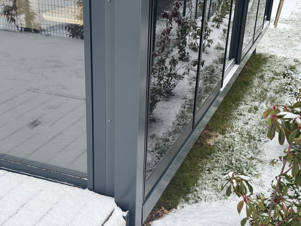 Pied de façade d'un module Hoummi sous la neige : bardage sombre, seuil et sol enneigé